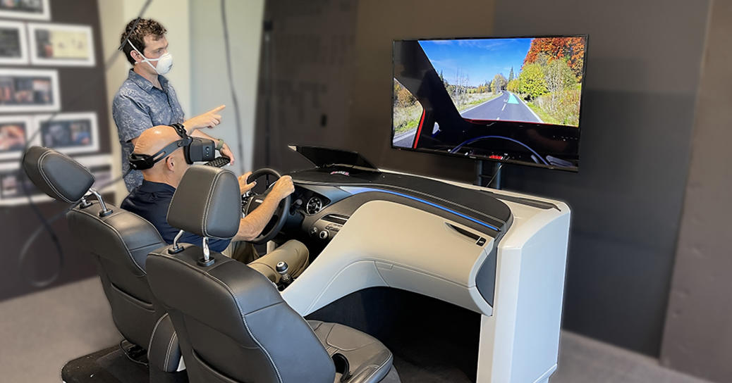 A man wearing VR goggles sits in a model vehicle cabin and tests a simulated driving experience 