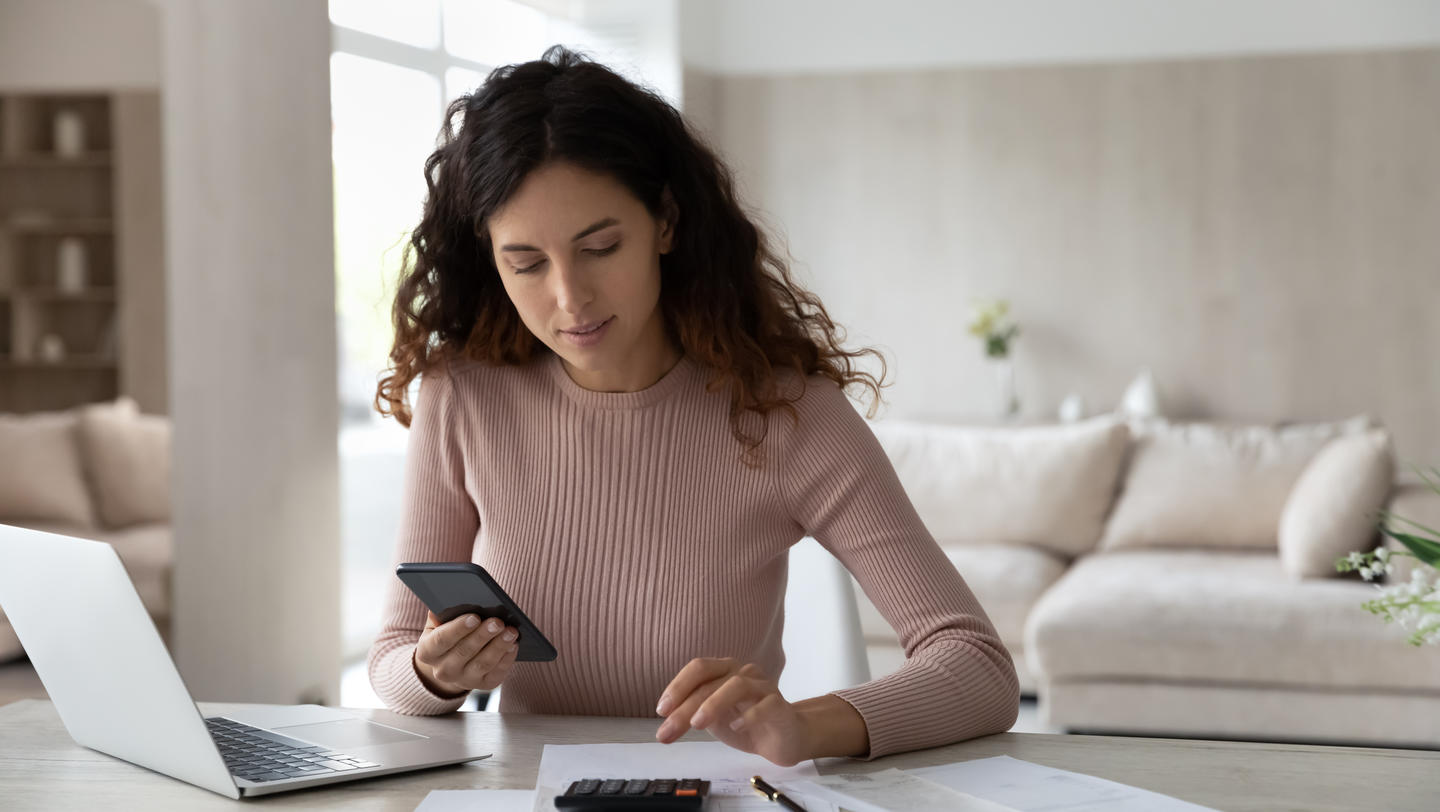 Latino woman pay bills on cell calculate on machine