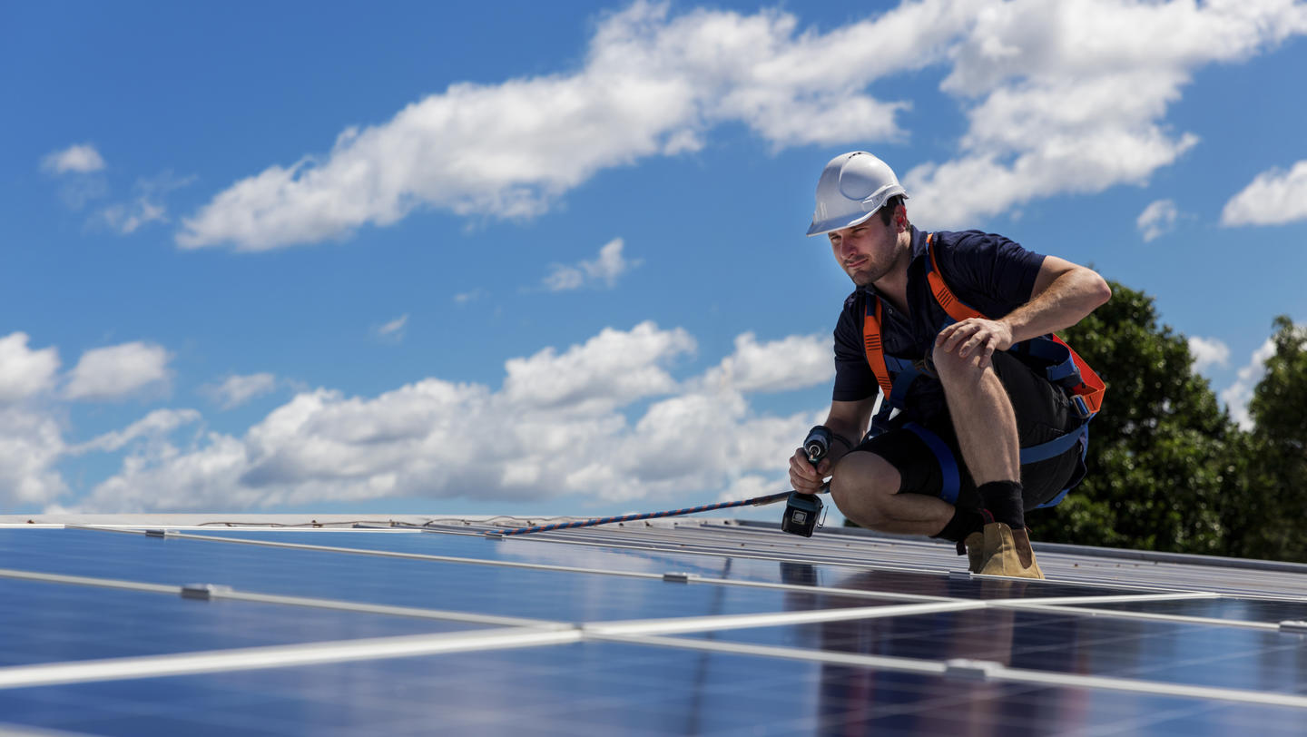 Technician with drill installing solar panels on roof